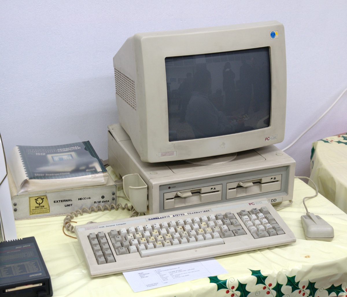 An Amstrad PC1512 with two 5.25-inch floppy drives, its monitor, keyboard, mouse and a joystick, on a display table