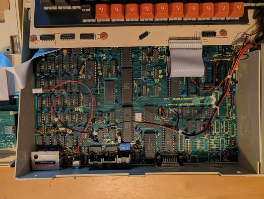 Inside the author's BBC Micro Model B with the lid removed, showing the green motherboard, ribbon cables and extra wiring, with a Raspberry Pi just visible at the left edge