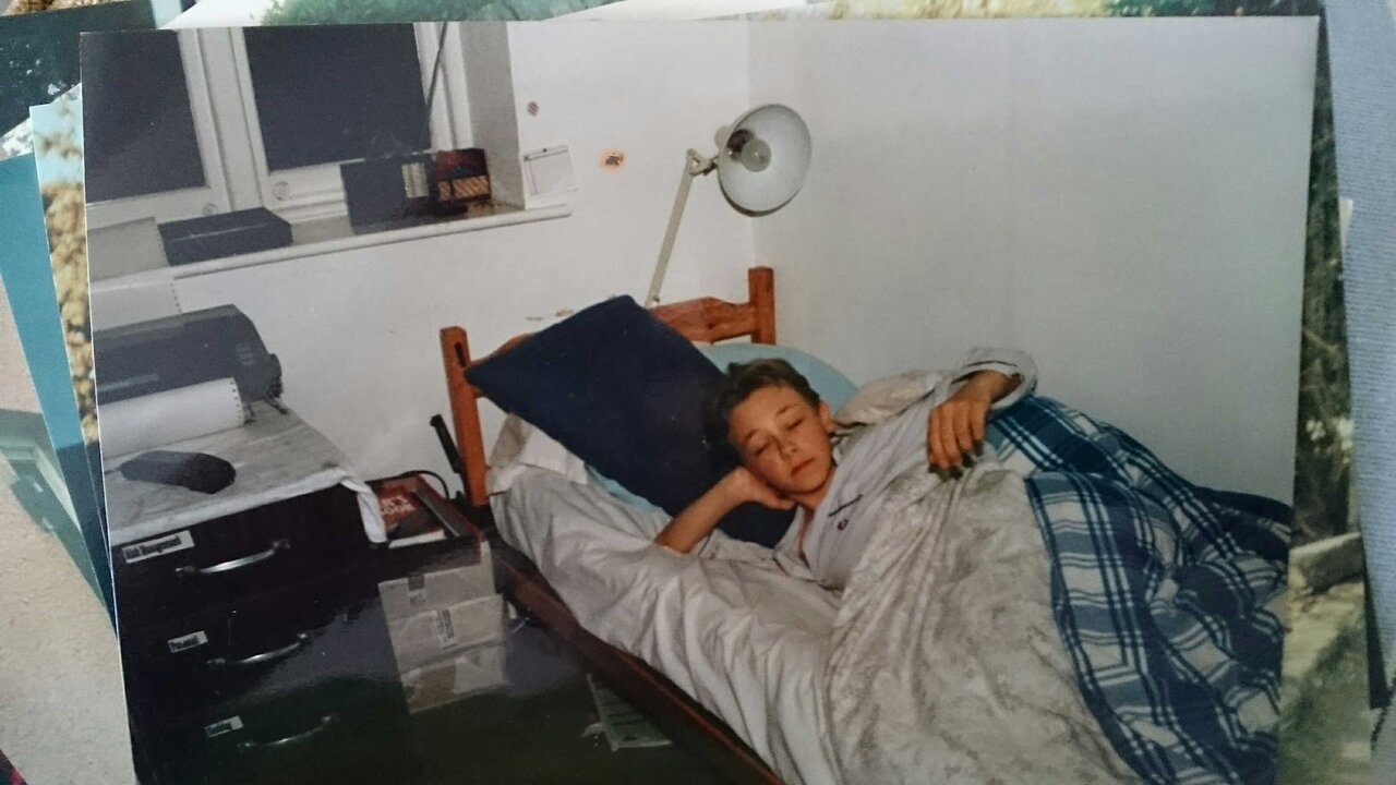 The author as a boy lying in bed, with the Amstrad DMP2160 printer and its tractor-feed paper on a chest of drawers beside the bed